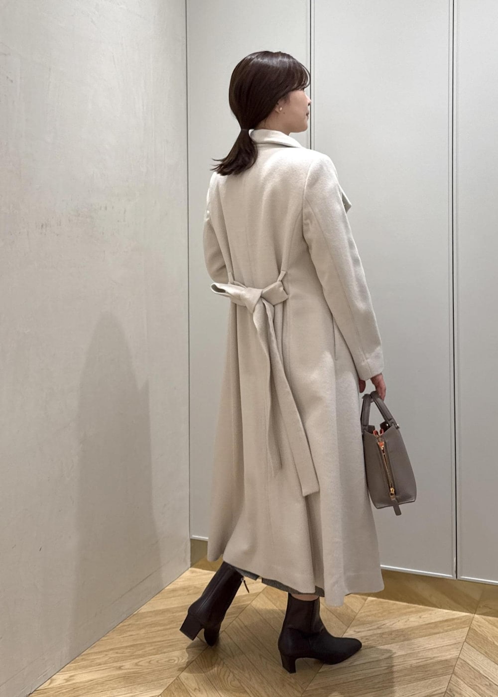 ブラウン系のブーツ、ブラウン系のハンドバッグ、ホワイト系のステンカラーコートを着用したレディースの秋コーディネートの3枚目の写真