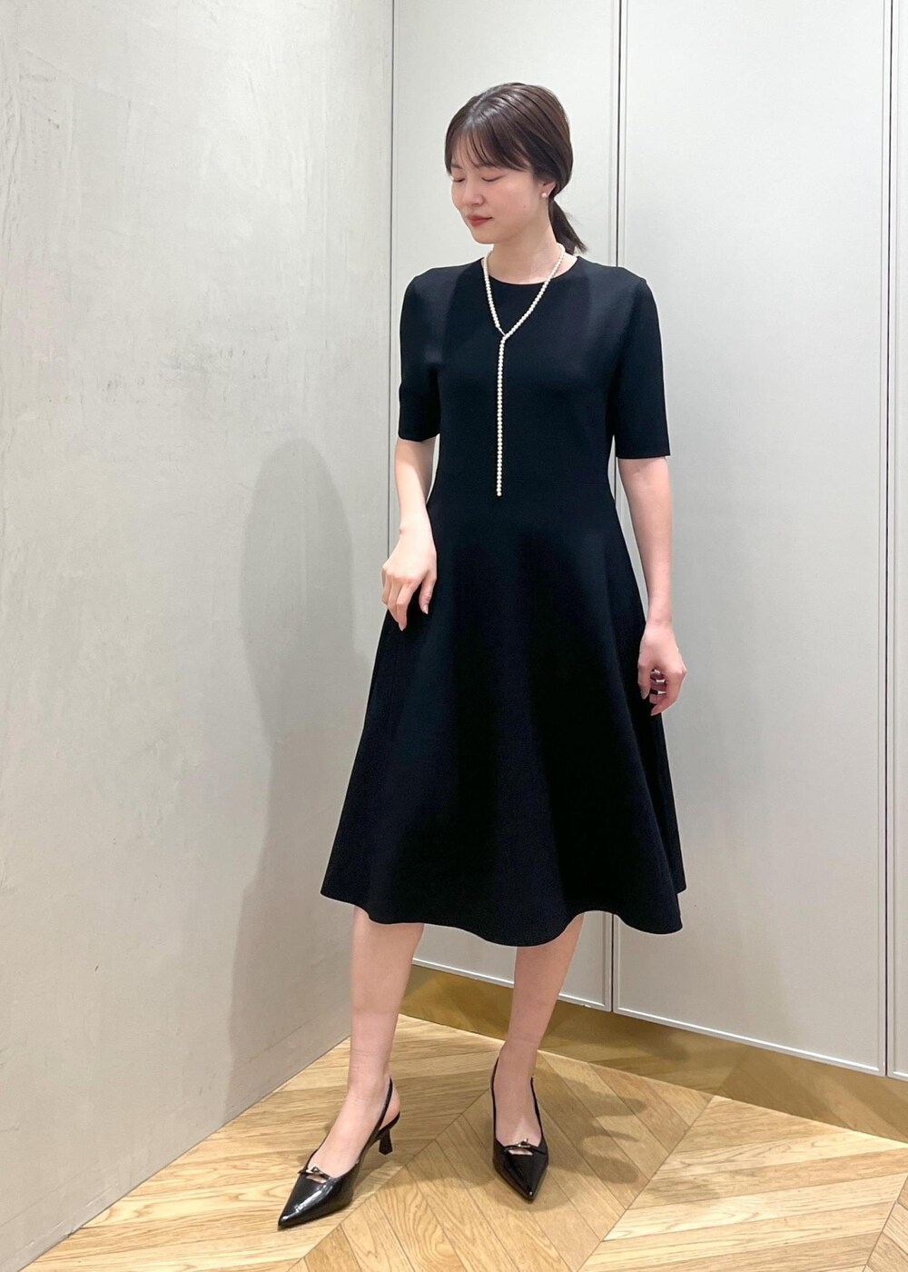 ブラック系のハンドバッグ、ブラック系のパンプス、ブルー系のワンピースを着用したレディースの冬コーディネートの6枚目の写真