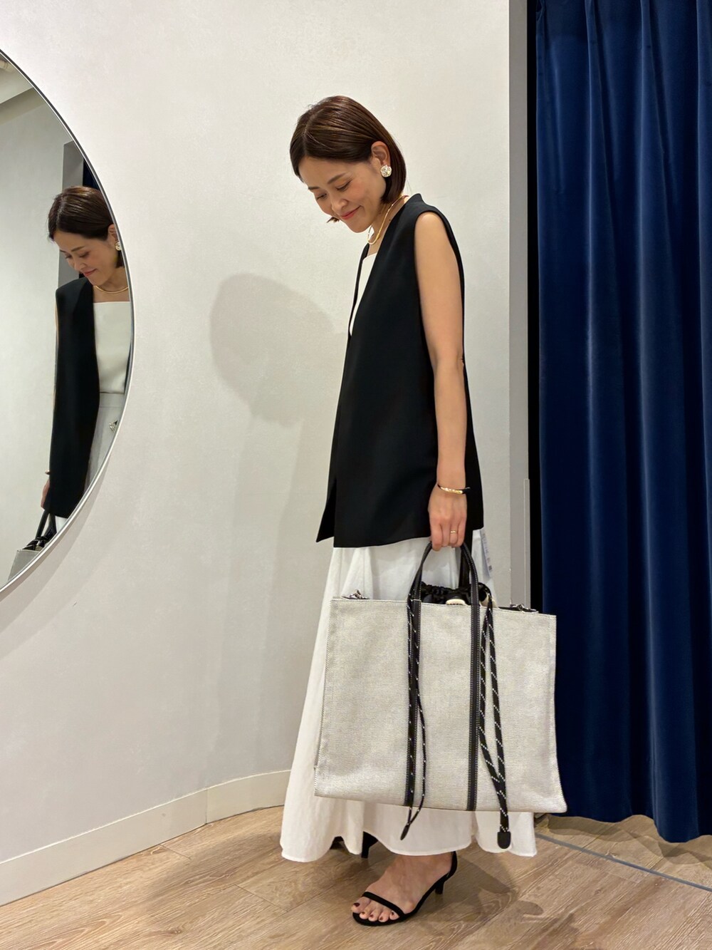 ブラック系のベスト、ホワイト系のキャミソール、ホワイト系のスカートを着用したレディースの夏コーディネートの5枚目の写真