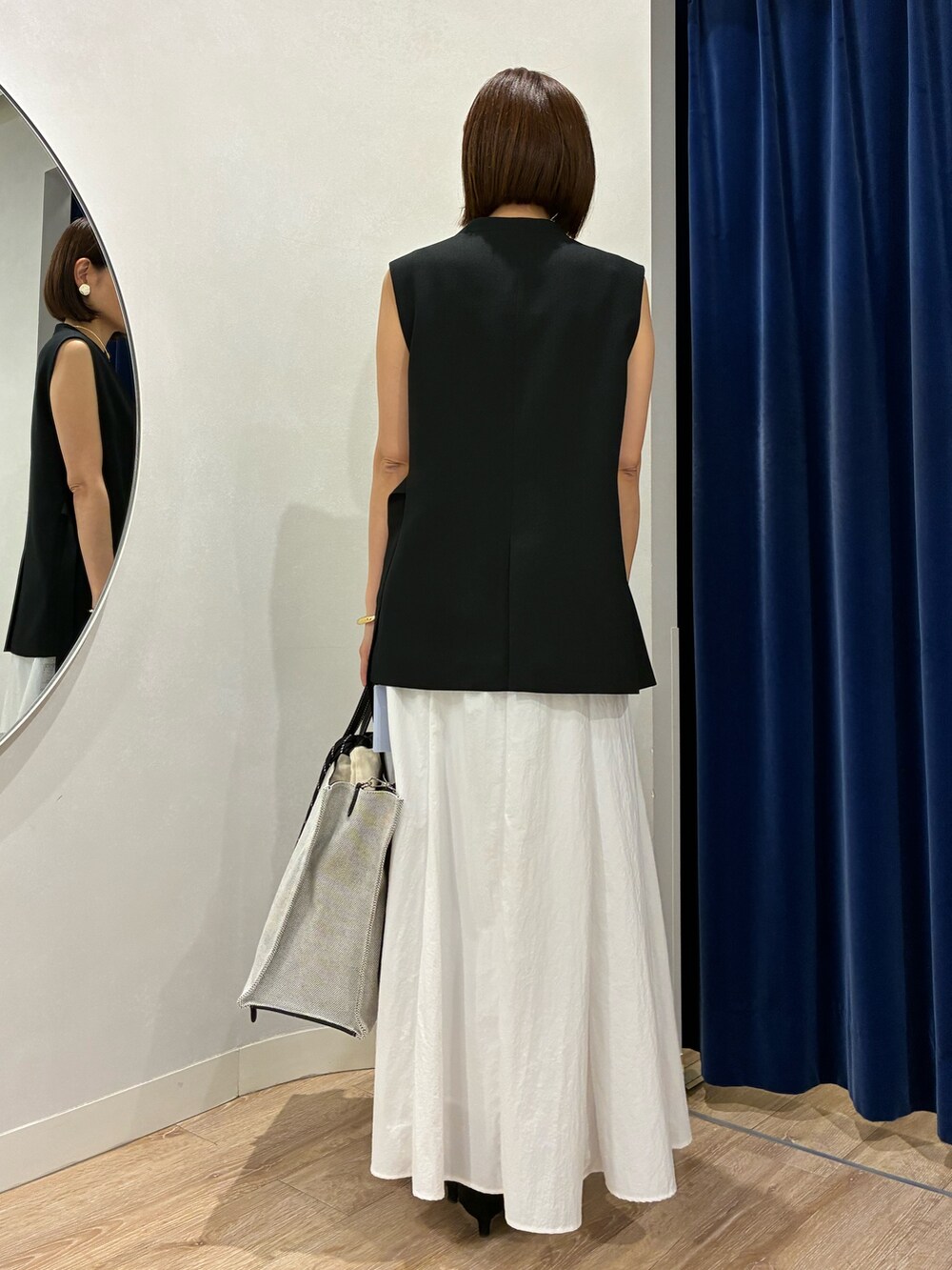 ブラック系のベスト、ホワイト系のキャミソール、ホワイト系のスカートを着用したレディースの夏コーディネートの6枚目の写真