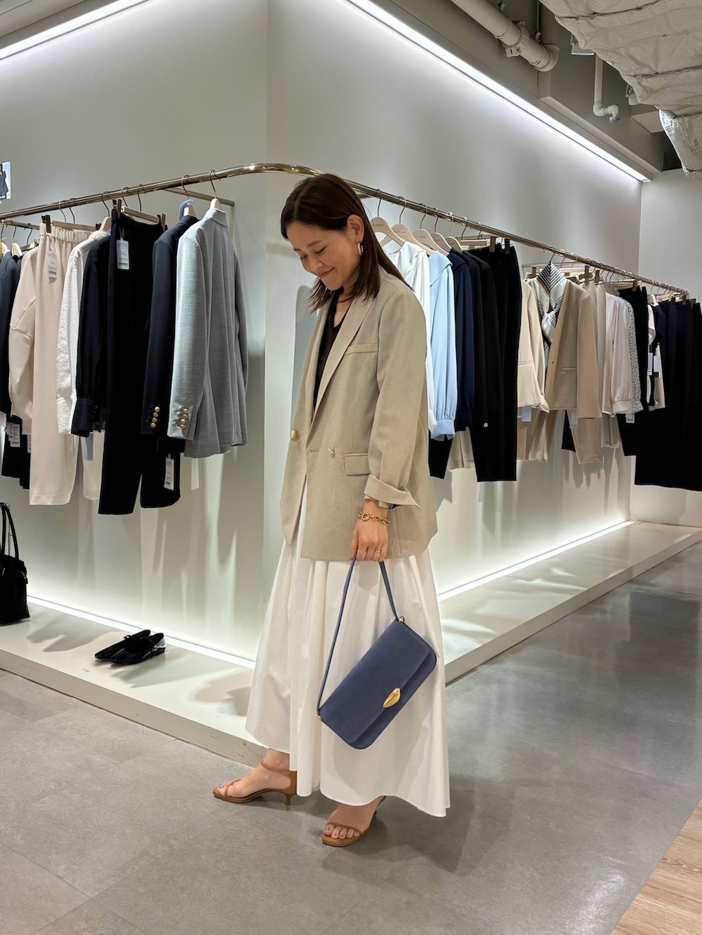 ベージュ系のテーラードジャケット、ホワイト系のスカート、ブラウン系のニット/セーターを着用したレディースの春コーディネートの2枚目の写真