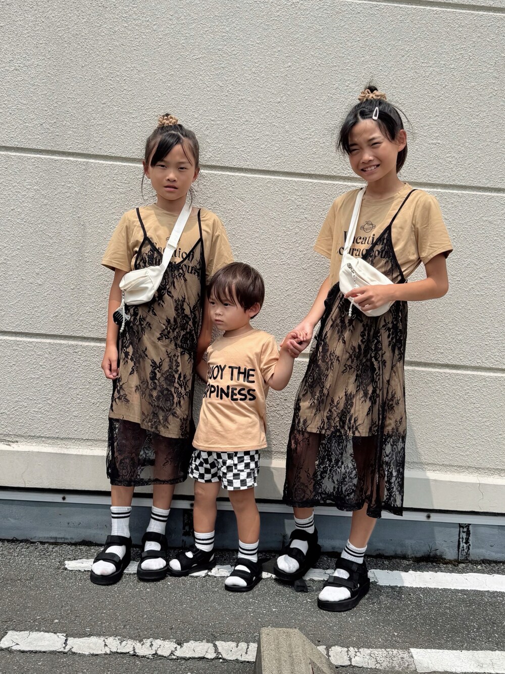 ベージュ系のTシャツ/カットソー、ベージュ系のワンピース、ブラック系のサンダルを着用したキッズの夏コーディネートの2枚目の写真