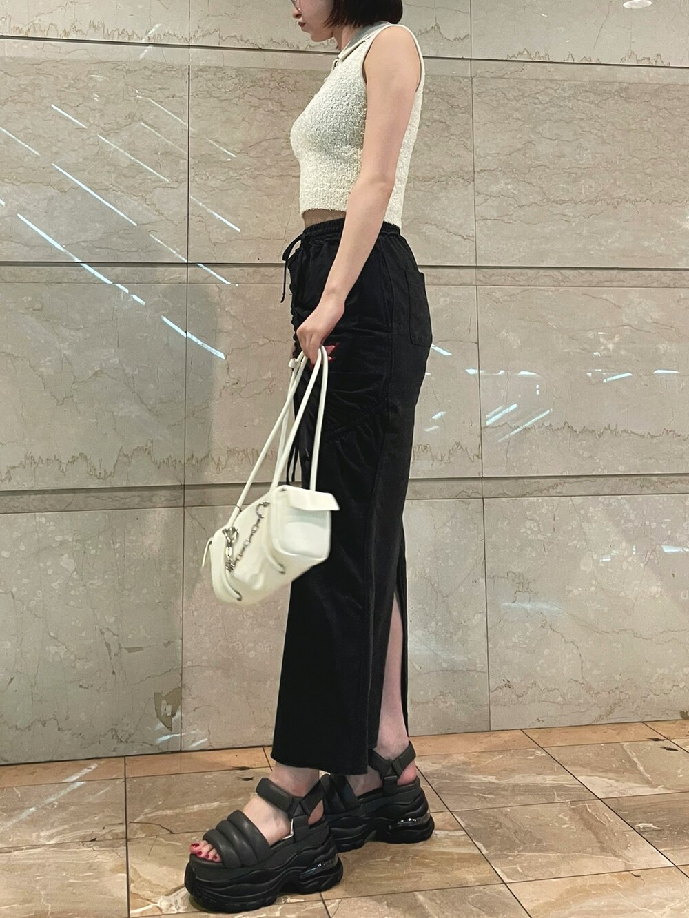 ホワイト系のニット/セーター、ブラック系のスカート、ホワイト系のハンドバッグを着用したレディースの夏コーディネートの3枚目の写真