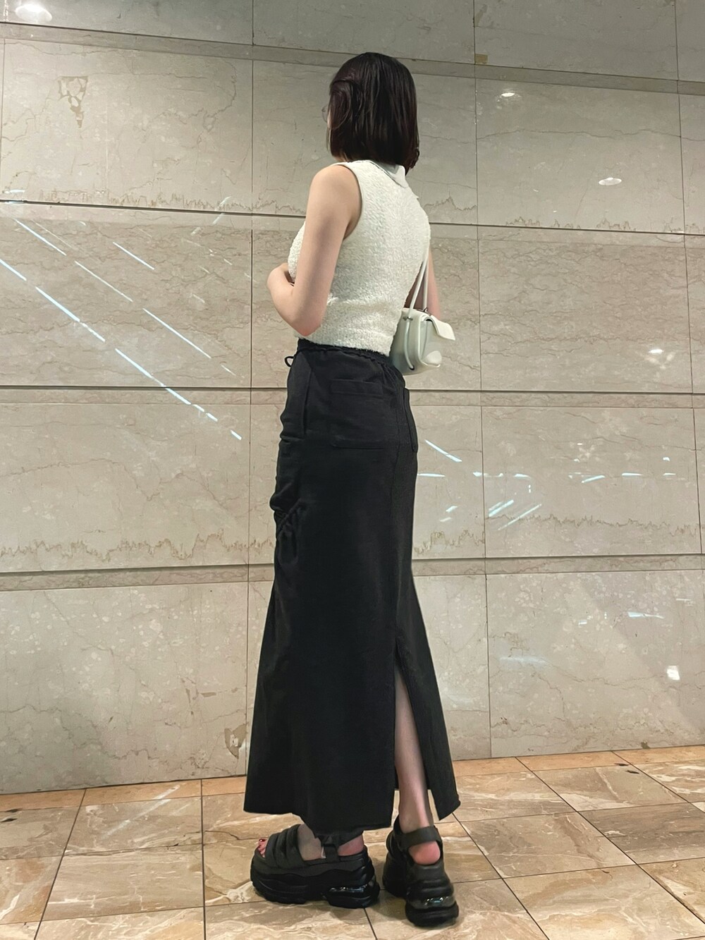 ホワイト系のニット/セーター、ブラック系のスカート、ホワイト系のハンドバッグを着用したレディースの夏コーディネートの2枚目の写真