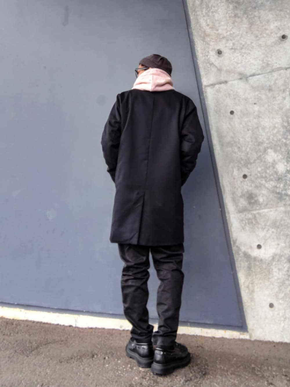 ブラック系のチェスターコート、ピンク系のパーカー、ブラック系のパンツを着用したメンズの春コーディネートの2枚目の写真