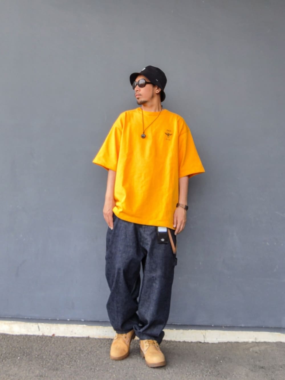 イエロー系のTシャツ/カットソー、ブルー系のデニムパンツ、イエロー系のブーツを着用したメンズの夏コーディネートの2枚目の写真