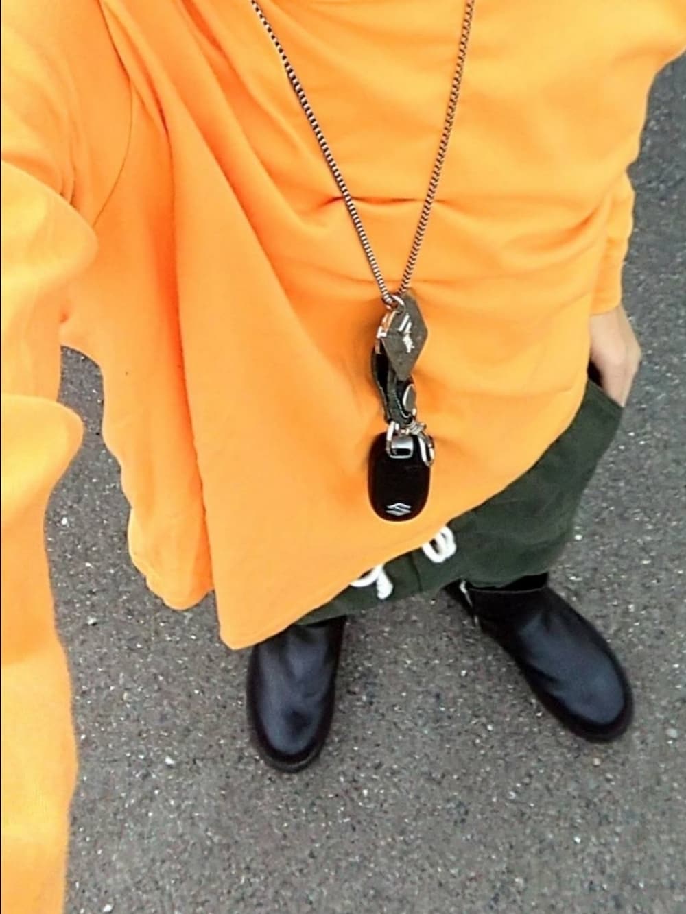 グリーン系のパンツ、ブラック系のブーツ、オレンジ系のTシャツ/カットソーを着用したメンズの冬コーディネートの3枚目の写真