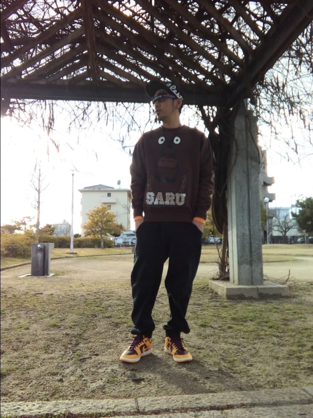 ブラウン系のスウェット、オレンジ系のTシャツ/カットソー、ブラック系のスウェットパンツを着用したメンズの春コーディネートの2枚目の写真