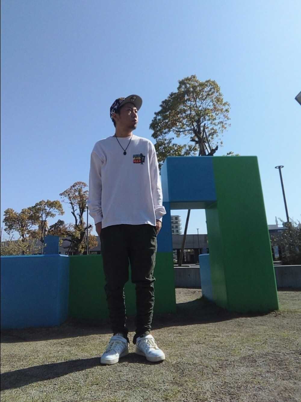 ピンク系のTシャツ/カットソー、グリーン系のパンツ、ホワイト系のスニーカーを着用したメンズの春コーディネートの2枚目の写真