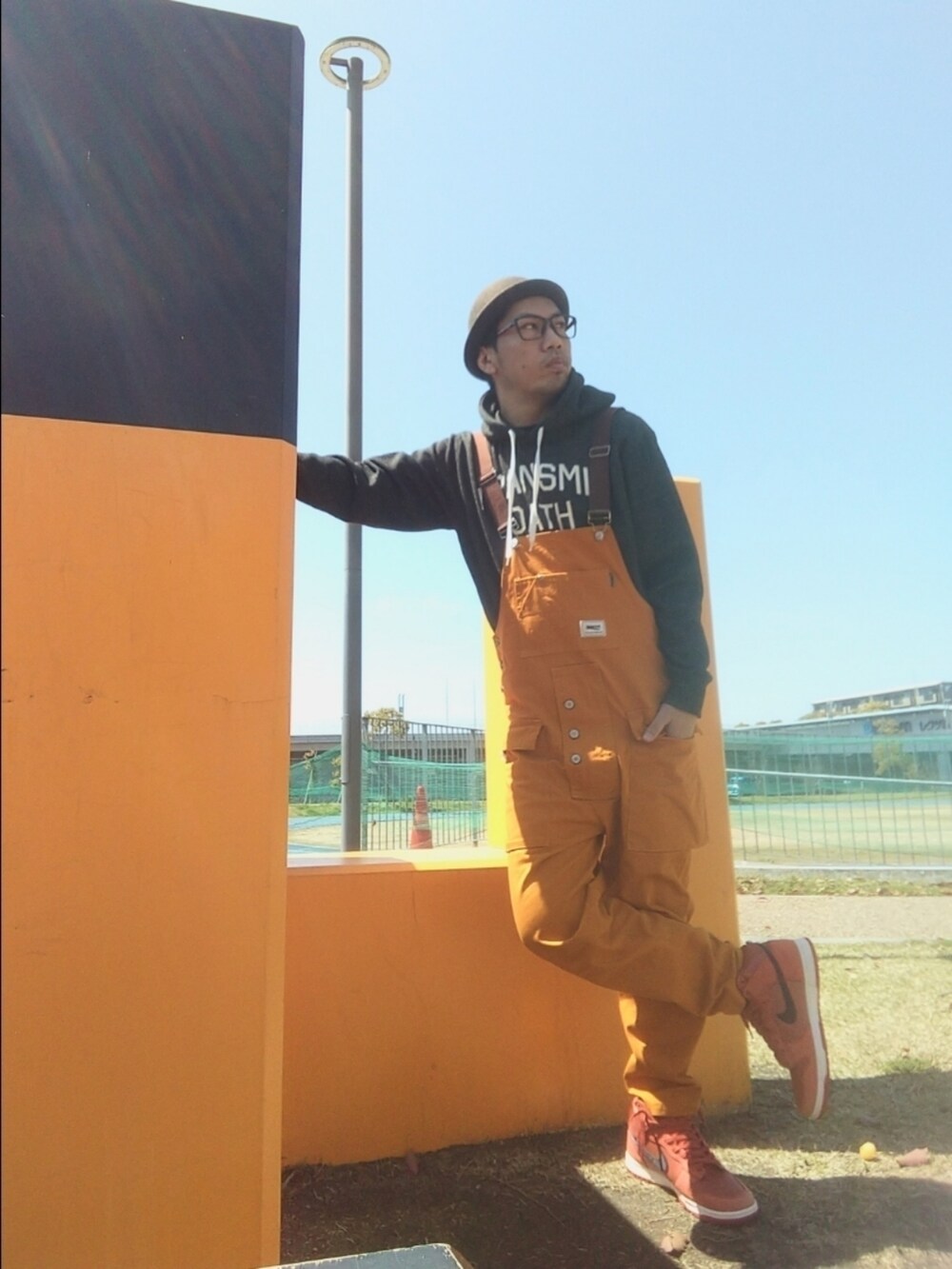 グレー系のパーカー、ブラウン系のサロペット/オーバーオール、オレンジ系のスニーカーを着用したメンズの春コーディネートの2枚目の写真