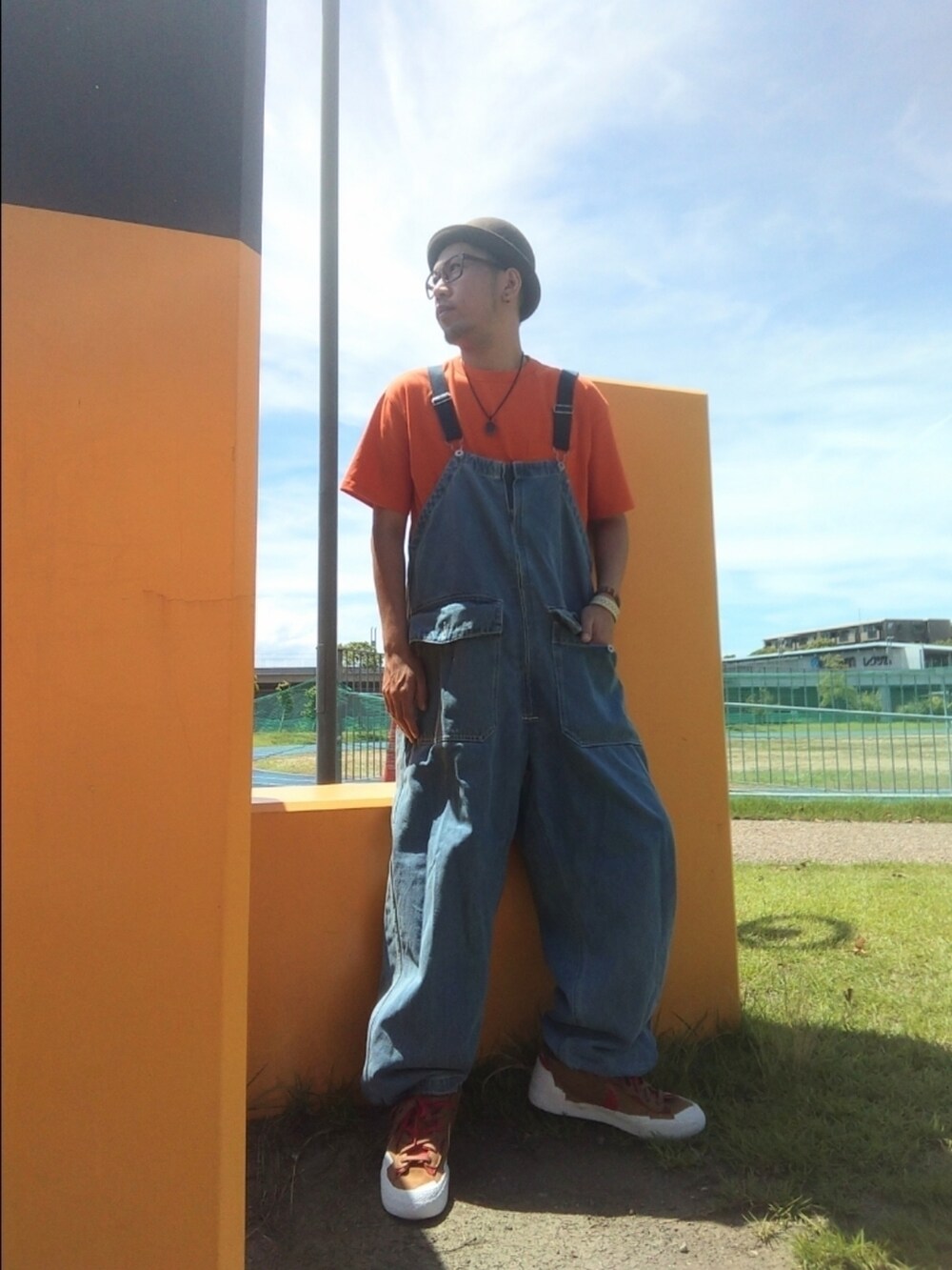 オレンジ系のTシャツ/カットソー、ブルー系のサロペット/オーバーオール、ブラウン系のスニーカーを着用したメンズの夏コーディネートの2枚目の写真