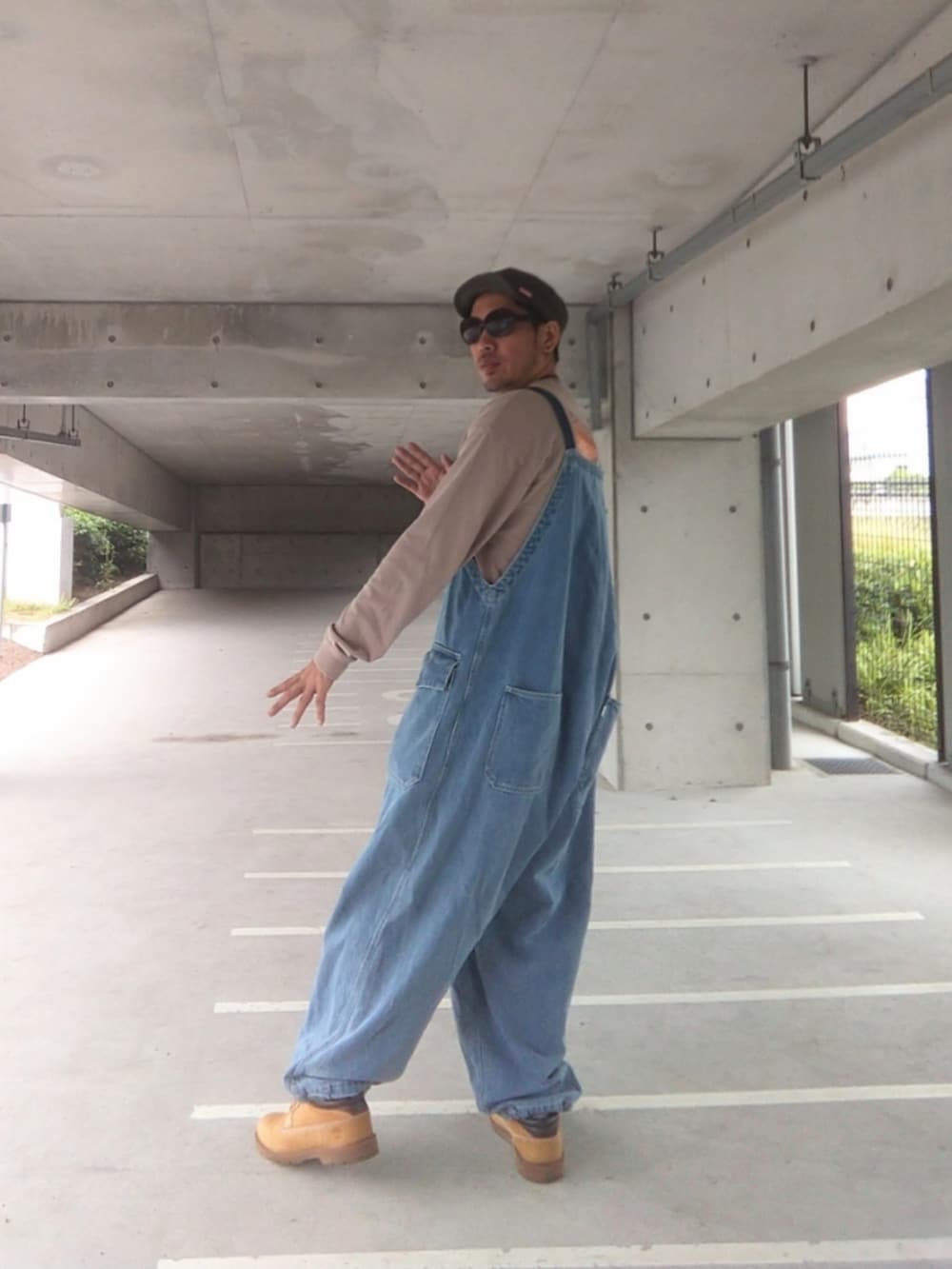 イエロー系のブーツ、ブルー系のサロペット/オーバーオール、ベージュ系のTシャツ/カットソーを着用したメンズの夏コーディネートの3枚目の写真