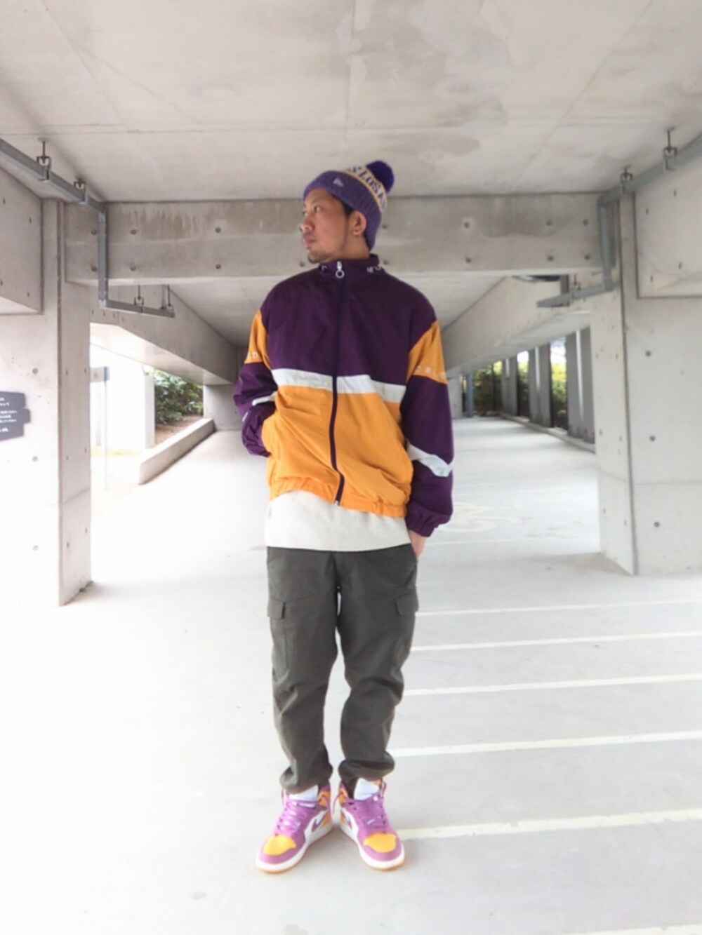 パープル系のナイロンジャケット、グリーン系のカーゴパンツ、イエロー系のスニーカーを着用したメンズの春コーディネートの2枚目の写真