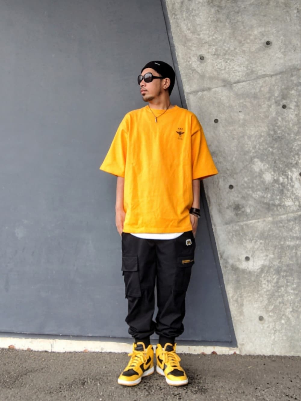 イエロー系のTシャツ/カットソー、ブラック系のカーゴパンツ、イエロー系のスニーカーを着用したメンズの夏コーディネートの3枚目の写真