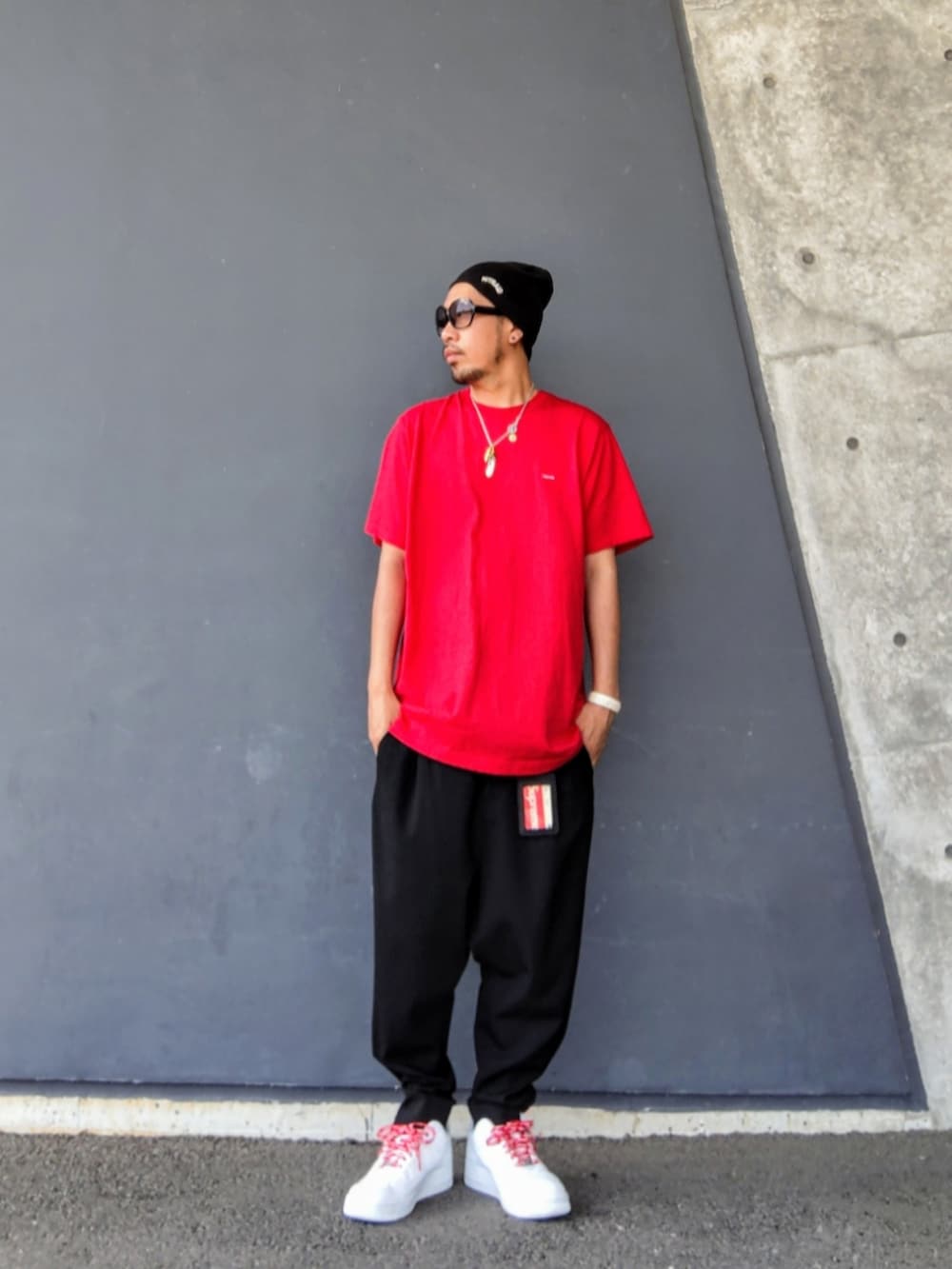 レッド系のTシャツ/カットソー、ブラック系のスラックス、ホワイト系のスニーカーを着用したメンズの夏コーディネートの2枚目の写真