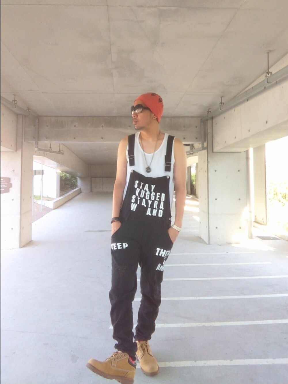 ブラック系のサロペット/オーバーオール、イエロー系のブーツ、オレンジ系のニットキャップ/ビーニーを着用したメンズの秋コーディネートの2枚目の写真