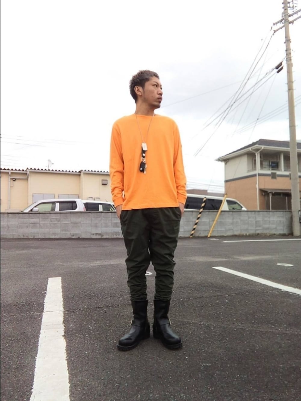グリーン系のパンツ、ブラック系のブーツ、オレンジ系のTシャツ/カットソーを着用したメンズの冬コーディネートの2枚目の写真