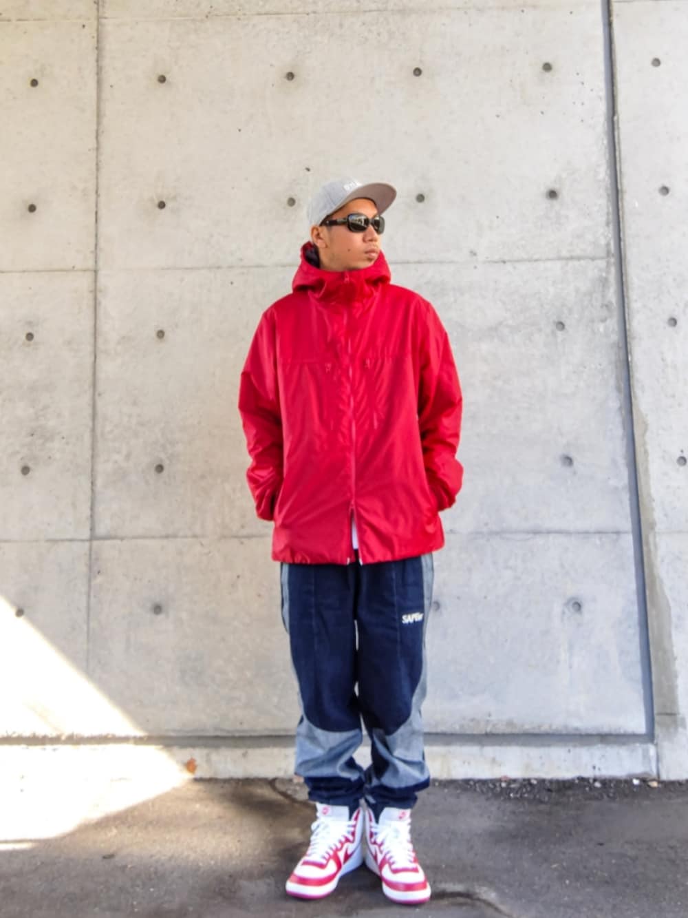 レッド系のナイロンジャケット、ブルー系のデニムパンツ、ホワイト系のスニーカーを着用したメンズの秋コーディネートの2枚目の写真