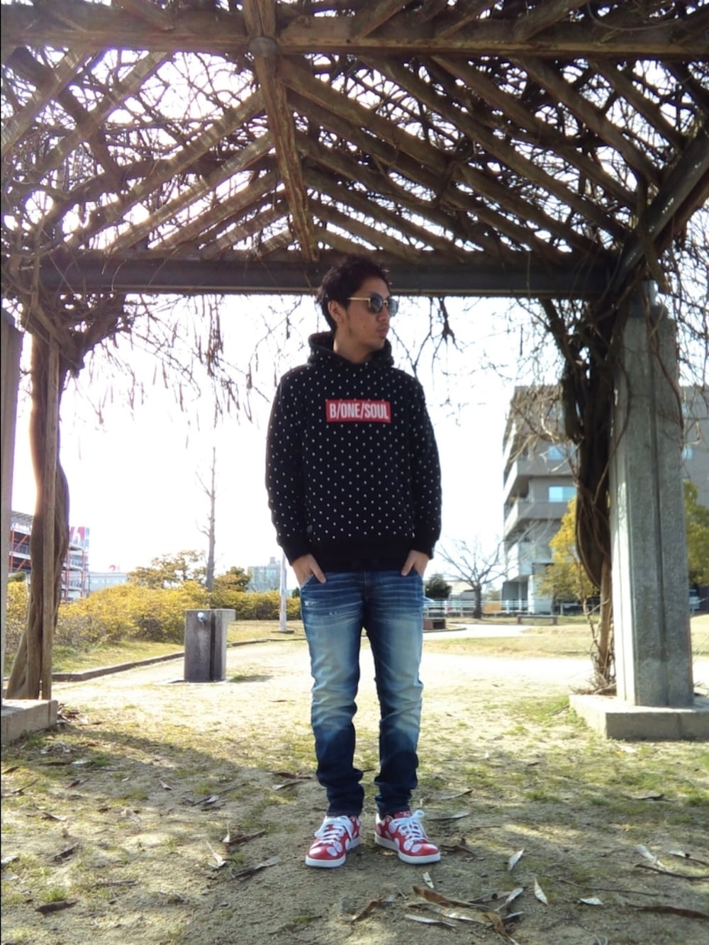 ブルー系のデニムパンツ、レッド系のスニーカー、ブラック系のパーカーを着用したメンズの春コーディネートの2枚目の写真