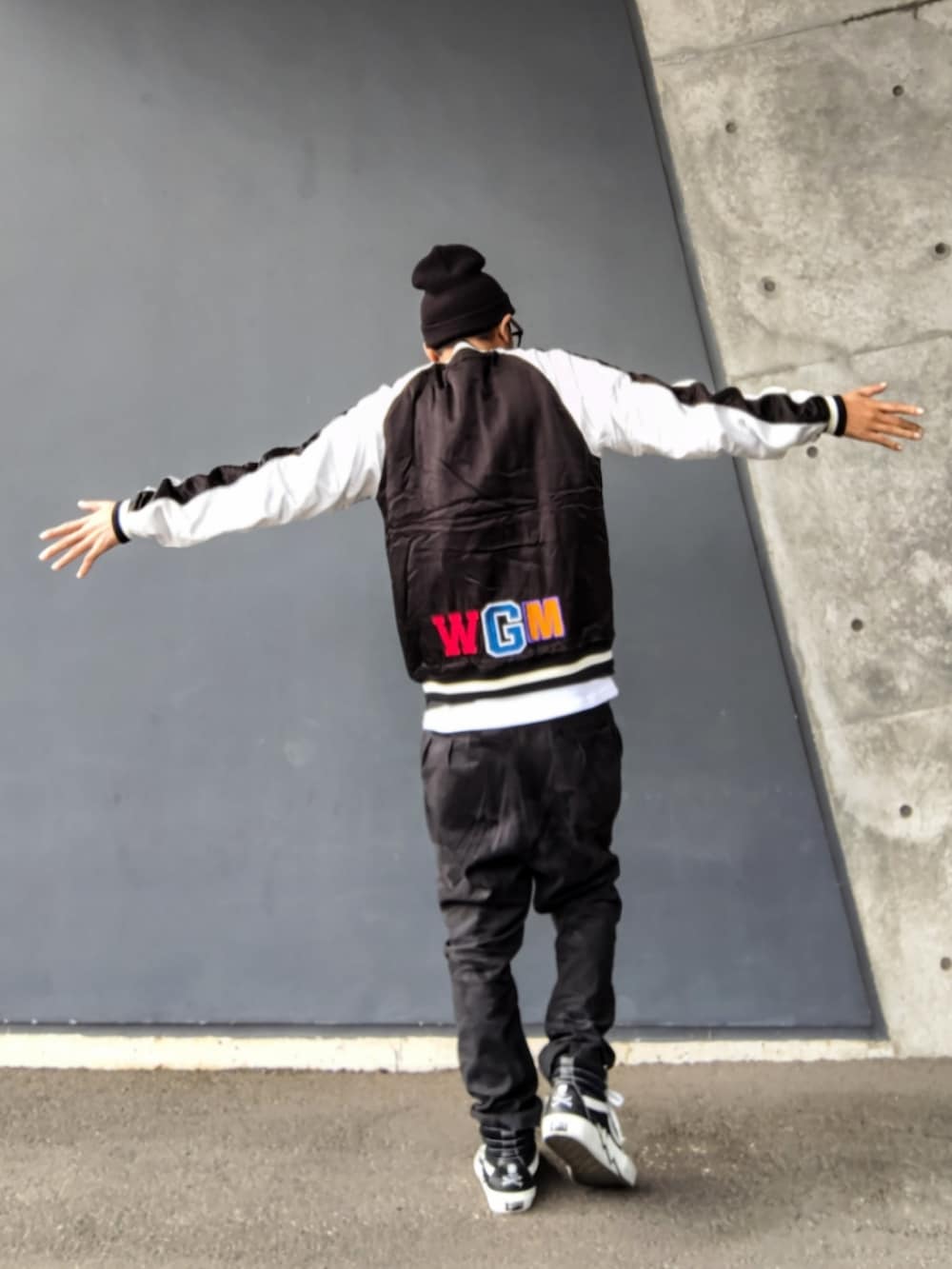 ブラック系のスカジャン、ブラック系のパンツ、ブラック系のスニーカーを着用したメンズの春コーディネートの3枚目の写真