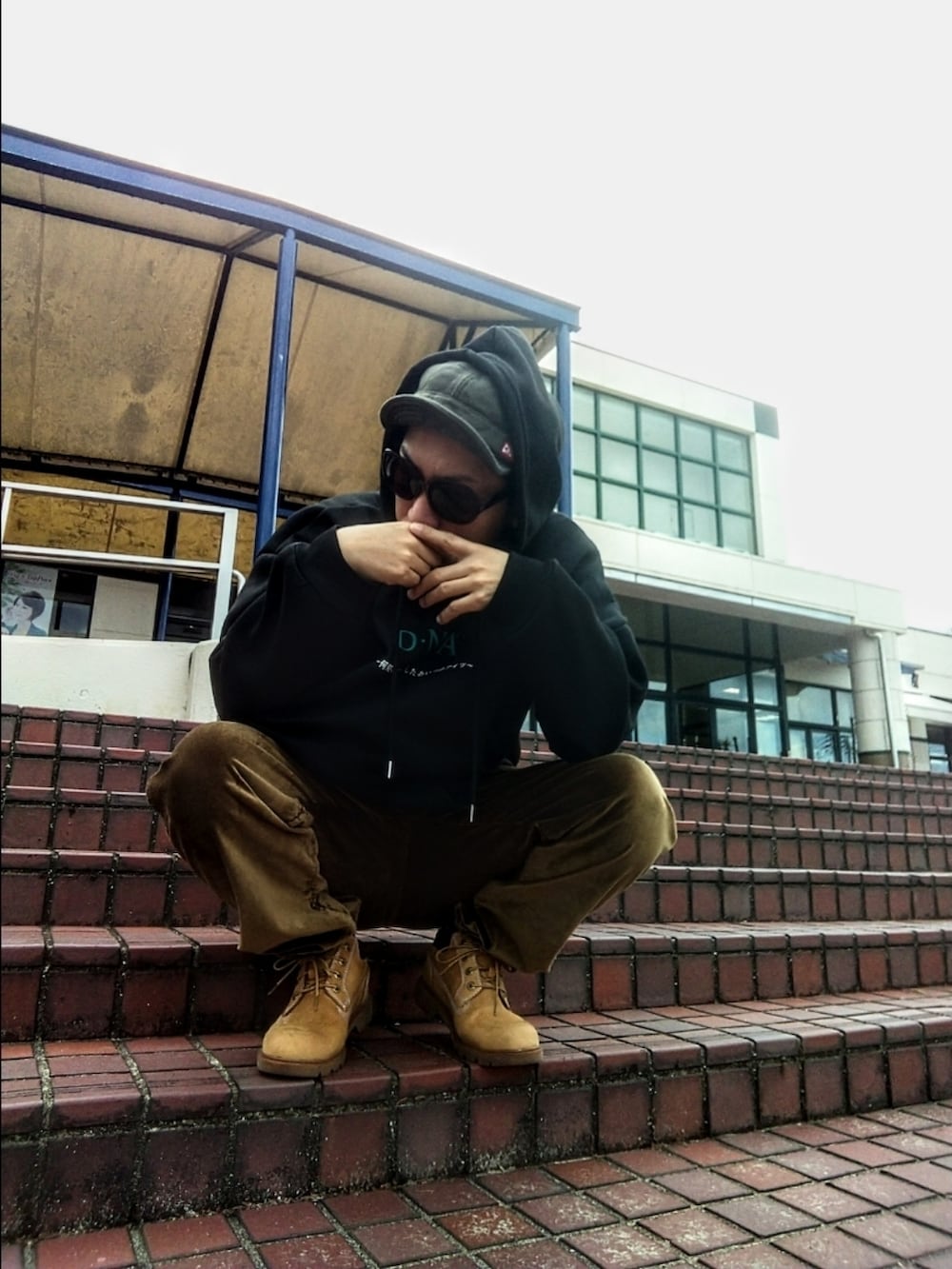 ブラック系のパーカー、ブラウン系のその他パンツ、イエロー系のブーツを着用したメンズの春コーディネートの2枚目の写真