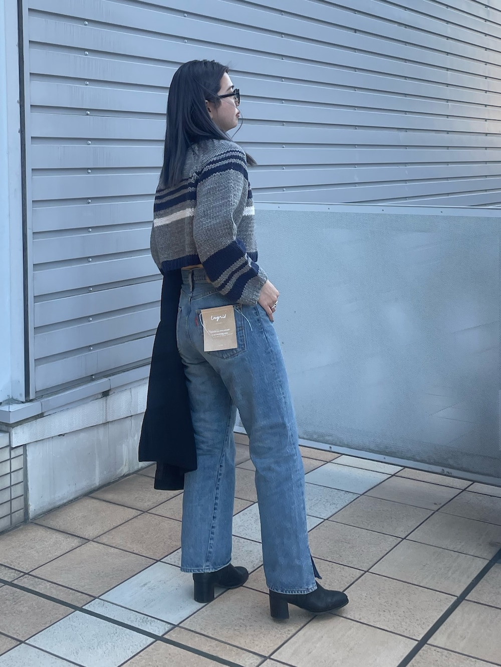 ブラック系のチェスターコート、ブルー系のデニムパンツ、グレー系のニット/セーターを着用したレディースの秋コーディネートの3枚目の写真