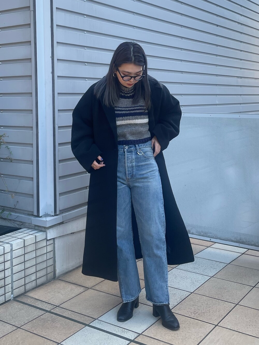 ブラック系のチェスターコート、ブルー系のデニムパンツ、グレー系のニット/セーターを着用したレディースの秋コーディネートの2枚目の写真