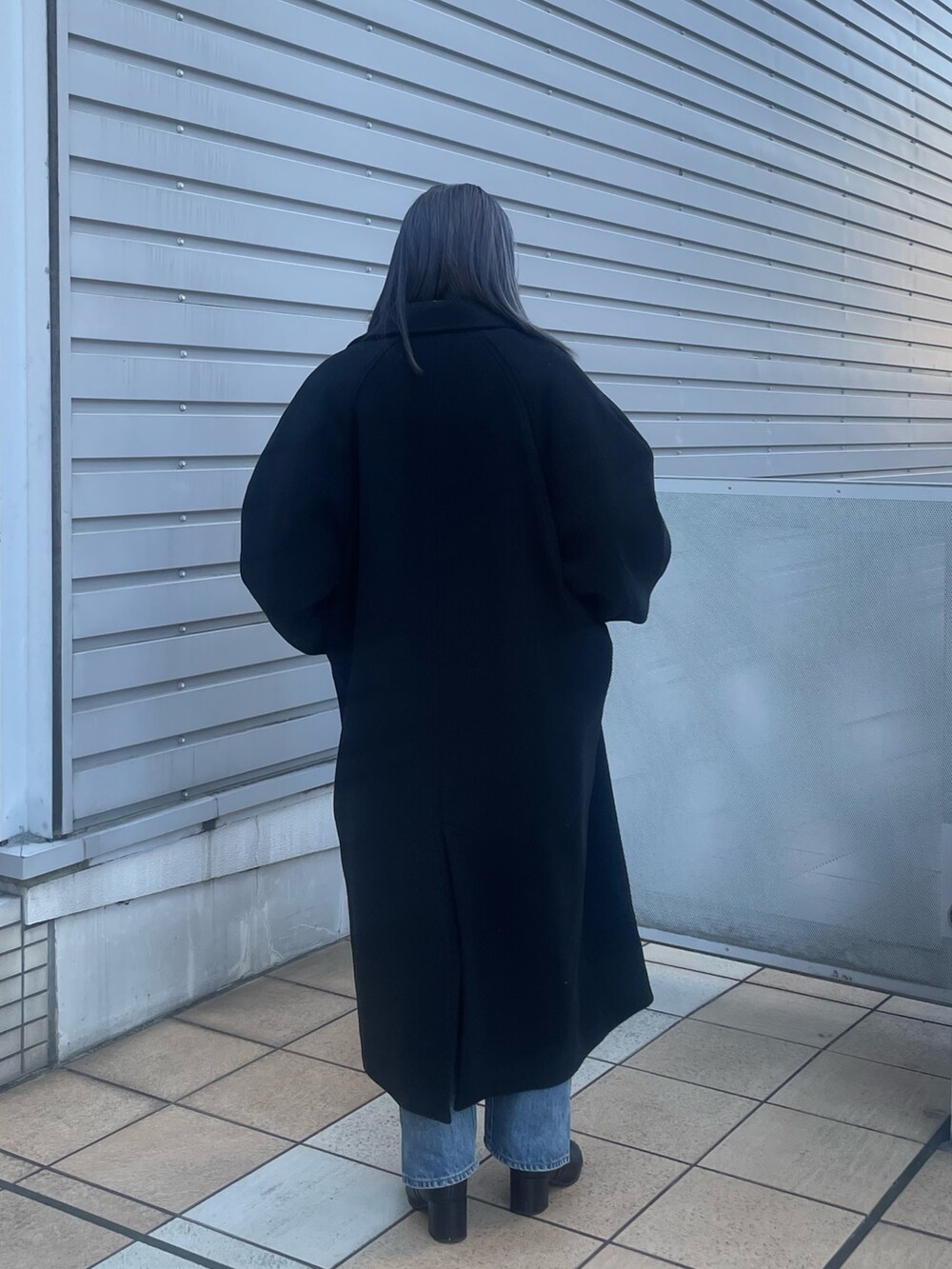 ブラック系のチェスターコート、ブルー系のデニムパンツ、グレー系のニット/セーターを着用したレディースの秋コーディネートの4枚目の写真