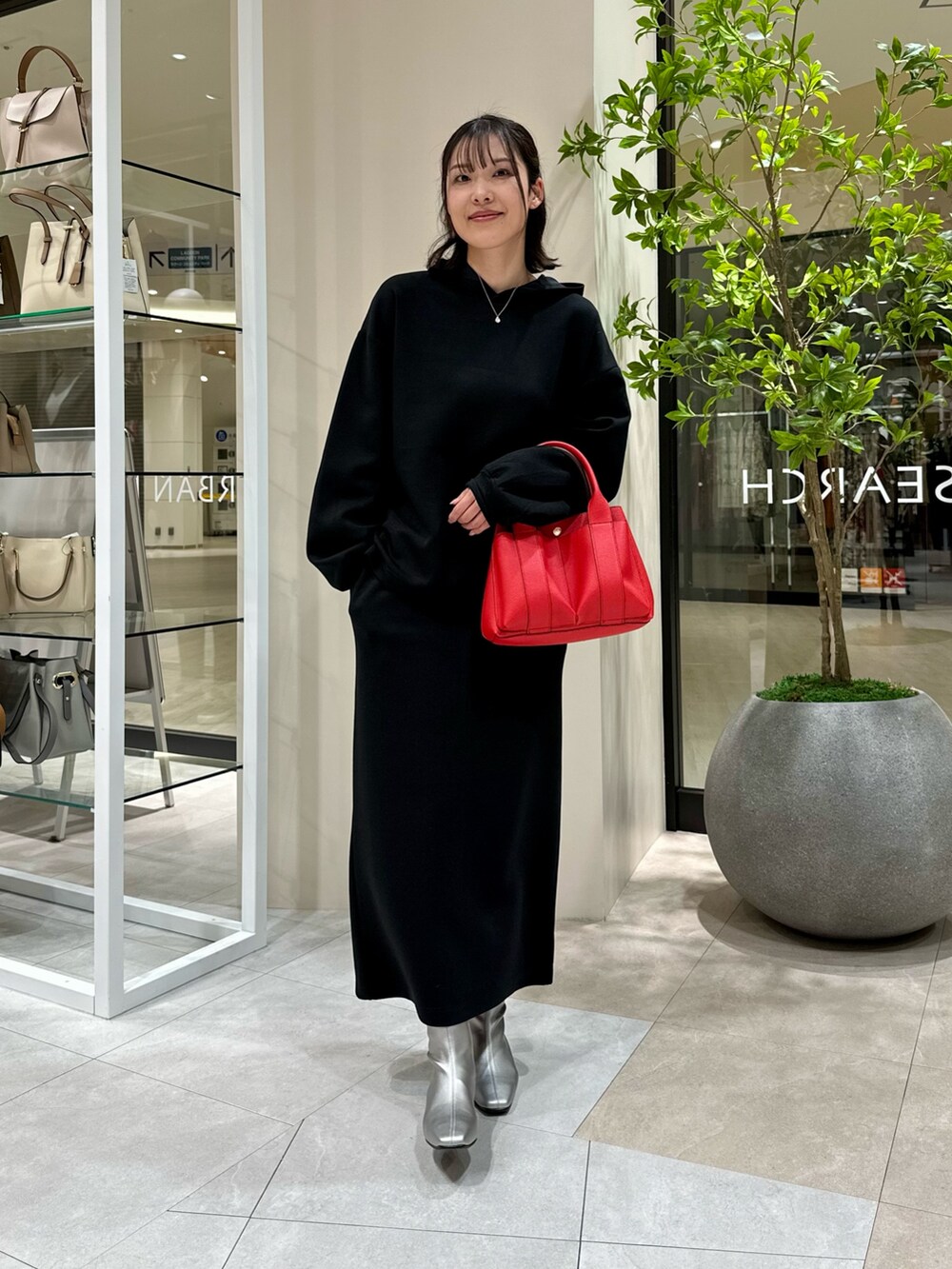 レッド系のトートバッグ、シルバー系のブーツ、ブラック系のワンピースを着用したレディースの冬コーディネートの2枚目の写真