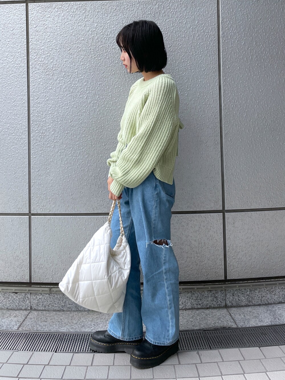 ホワイト系のトートバッグ、ブラック系のブーツ、ブルー系のデニムパンツを着用したレディースの秋コーディネートの2枚目の写真