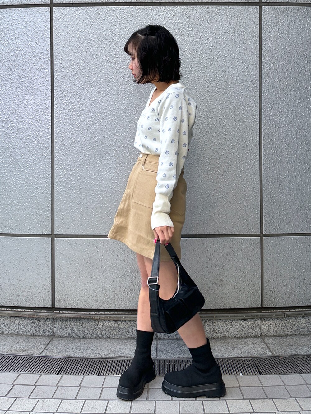 ブラック系のショルダーバッグ、ベージュ系のスカート、ホワイト系のニット/セーターを着用したレディースの冬コーディネートの2枚目の写真