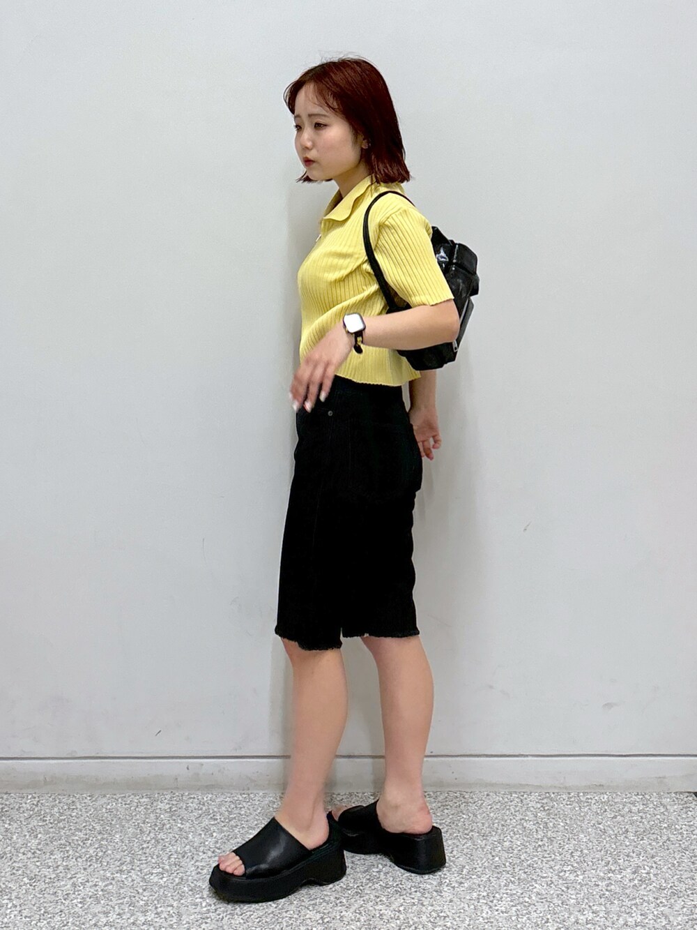 イエロー系のニット/セーター、ブラック系のデニムパンツ、ホワイト系のハンドバッグを着用したレディースの夏コーディネートの2枚目の写真