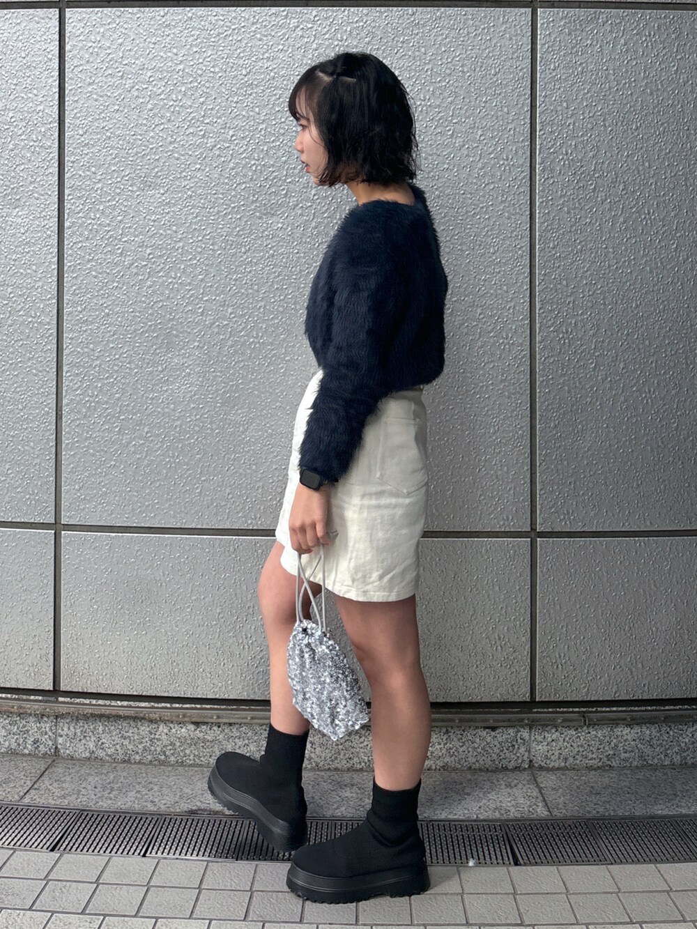 シルバー系のハンドバッグ、ブルー系のカーディガン/ボレロ、ホワイト系のスカートを着用したレディースの冬コーディネートの2枚目の写真