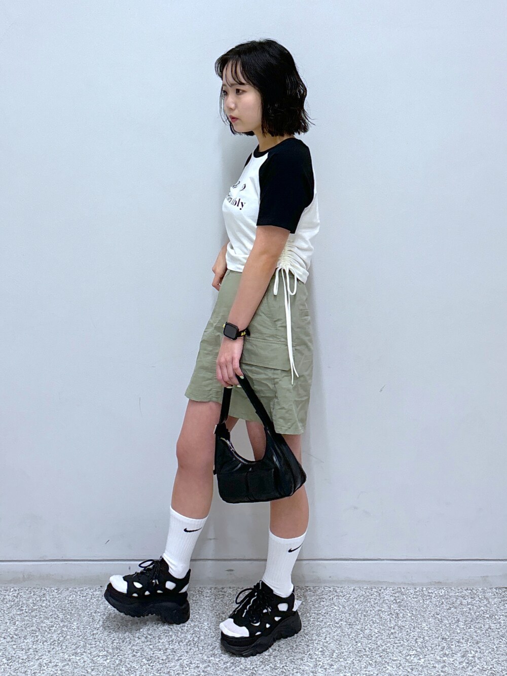 ブラック系のショルダーバッグ、ブラック系のサンダル、グリーン系のスカートを着用したレディースの春コーディネートの3枚目の写真