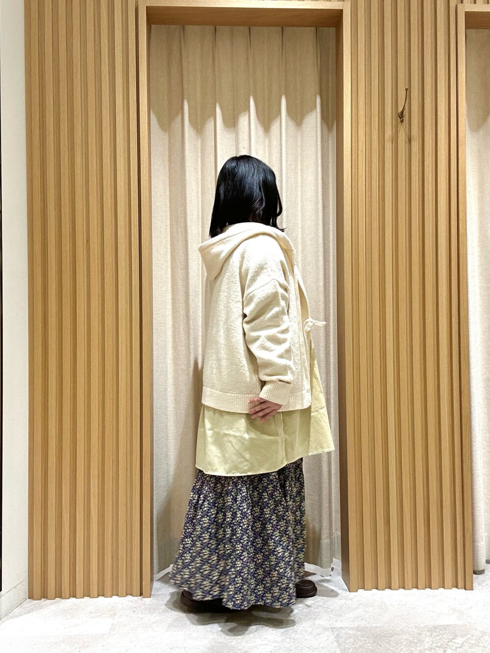 イエロー系のシャツ/ブラウス、ホワイト系のカーディガン/ボレロ、ブルー系のスカートを着用したレディースの冬コーディネートの2枚目の写真