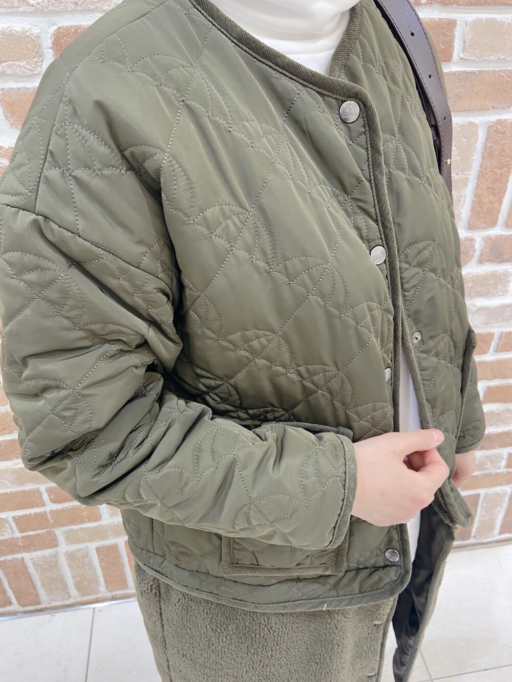 グリーン系のノーカラーコート、ブラック系のチノパンツ、ベージュ系のショルダーバッグを着用したレディースの秋コーディネートの3枚目の写真