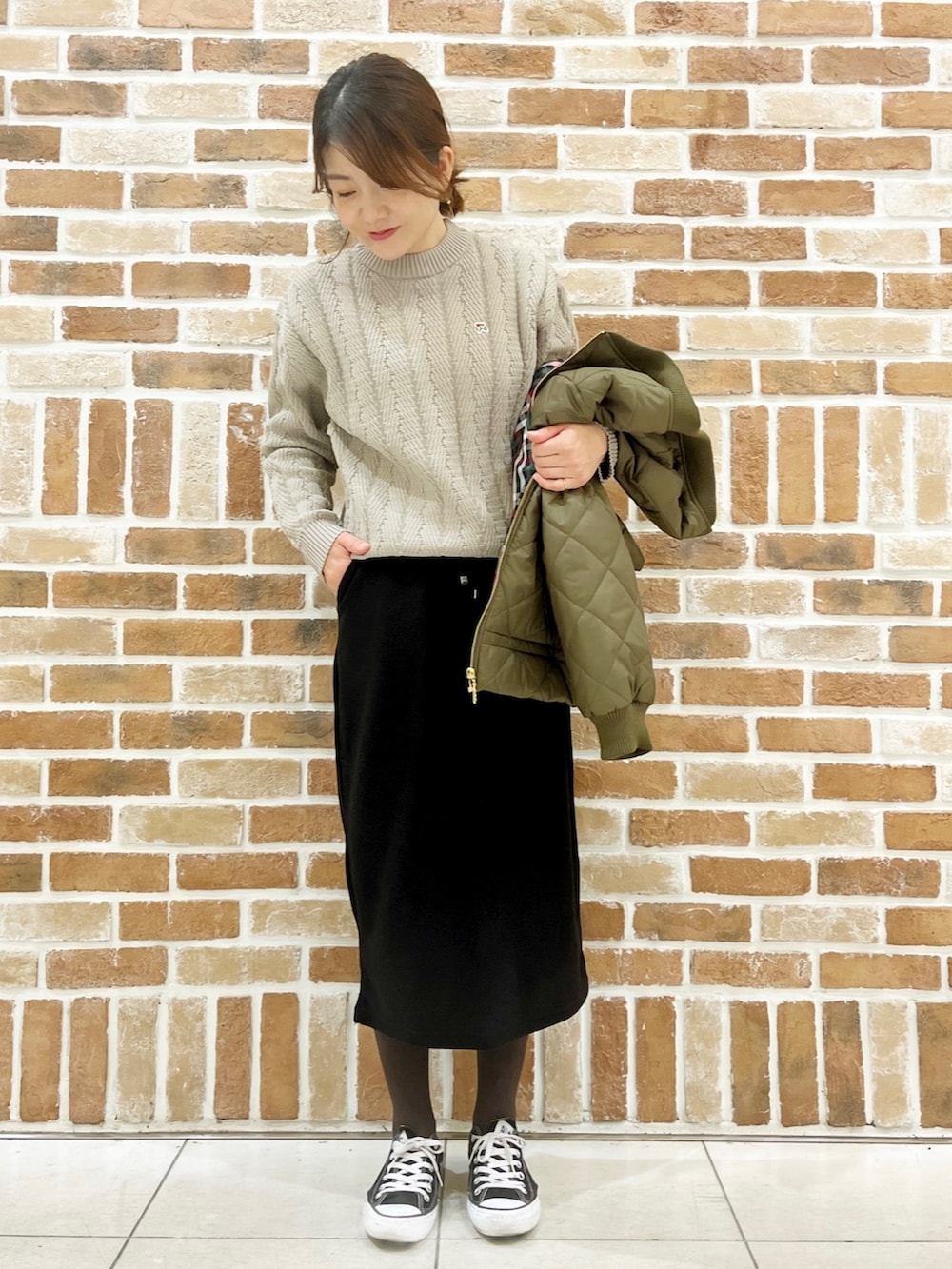 グリーン系のミリタリージャケット、ベージュ系のニット/セーター、ブラック系のスカートを着用したレディースの秋コーディネートの2枚目の写真