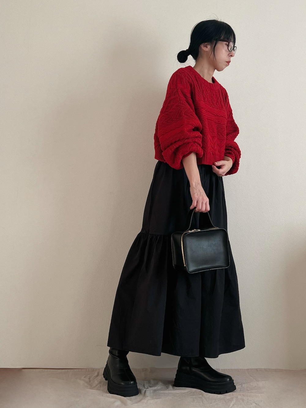 レッド系のニット/セーター、ブラック系のスカート、ブラック系のブーツを着用したレディースの冬コーディネートの2枚目の写真