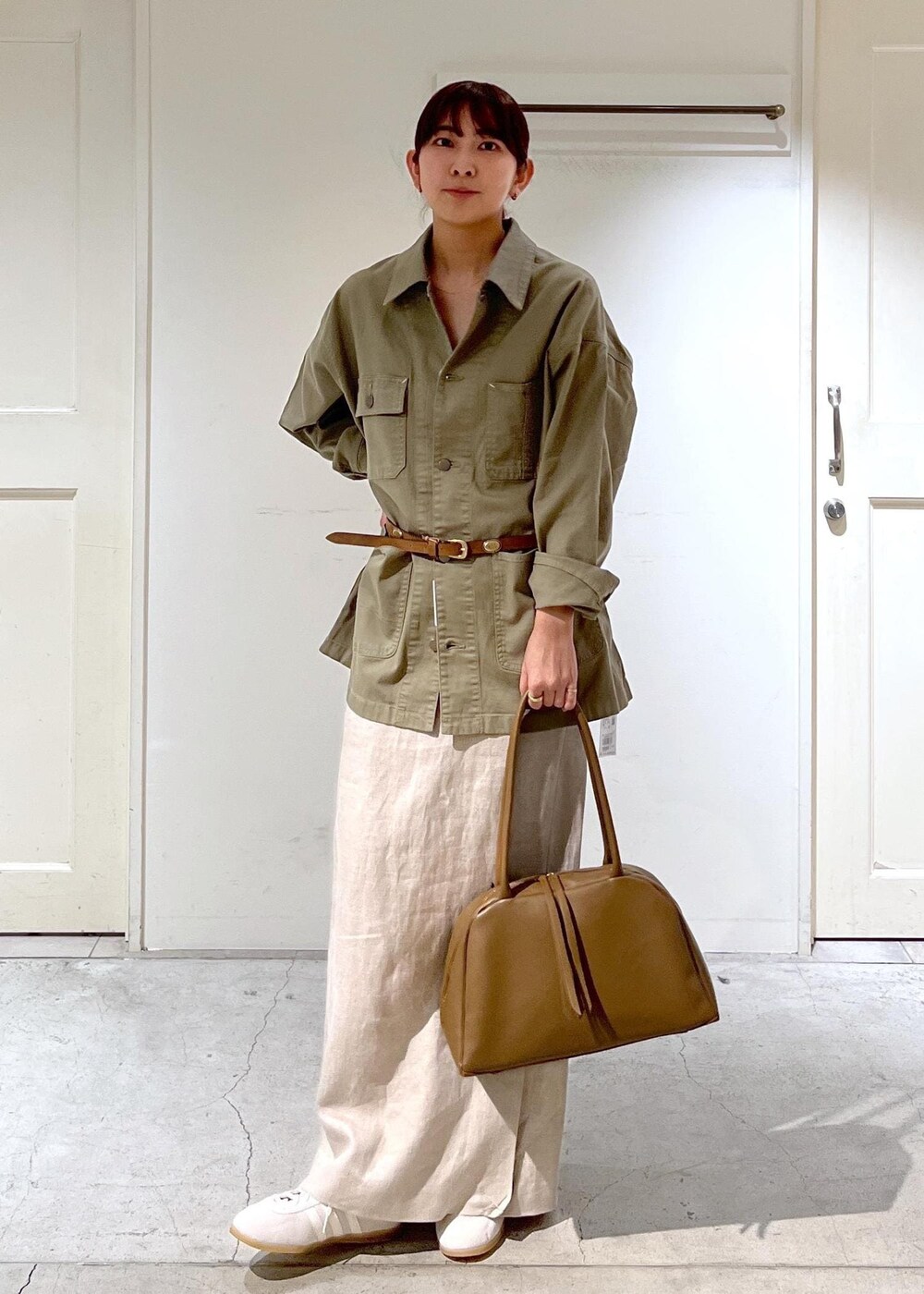 ブラウン系のボストンバッグ、ベージュ系のスカート、グリーン系のカバーオールを着用したレディースの春コーディネートの2枚目の写真