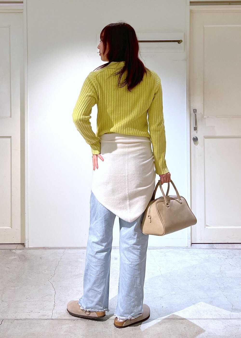 ベージュ系のボストンバッグ、イエロー系のニット/セーター、ブルー系のデニムパンツを着用したレディースの冬コーディネートの3枚目の写真