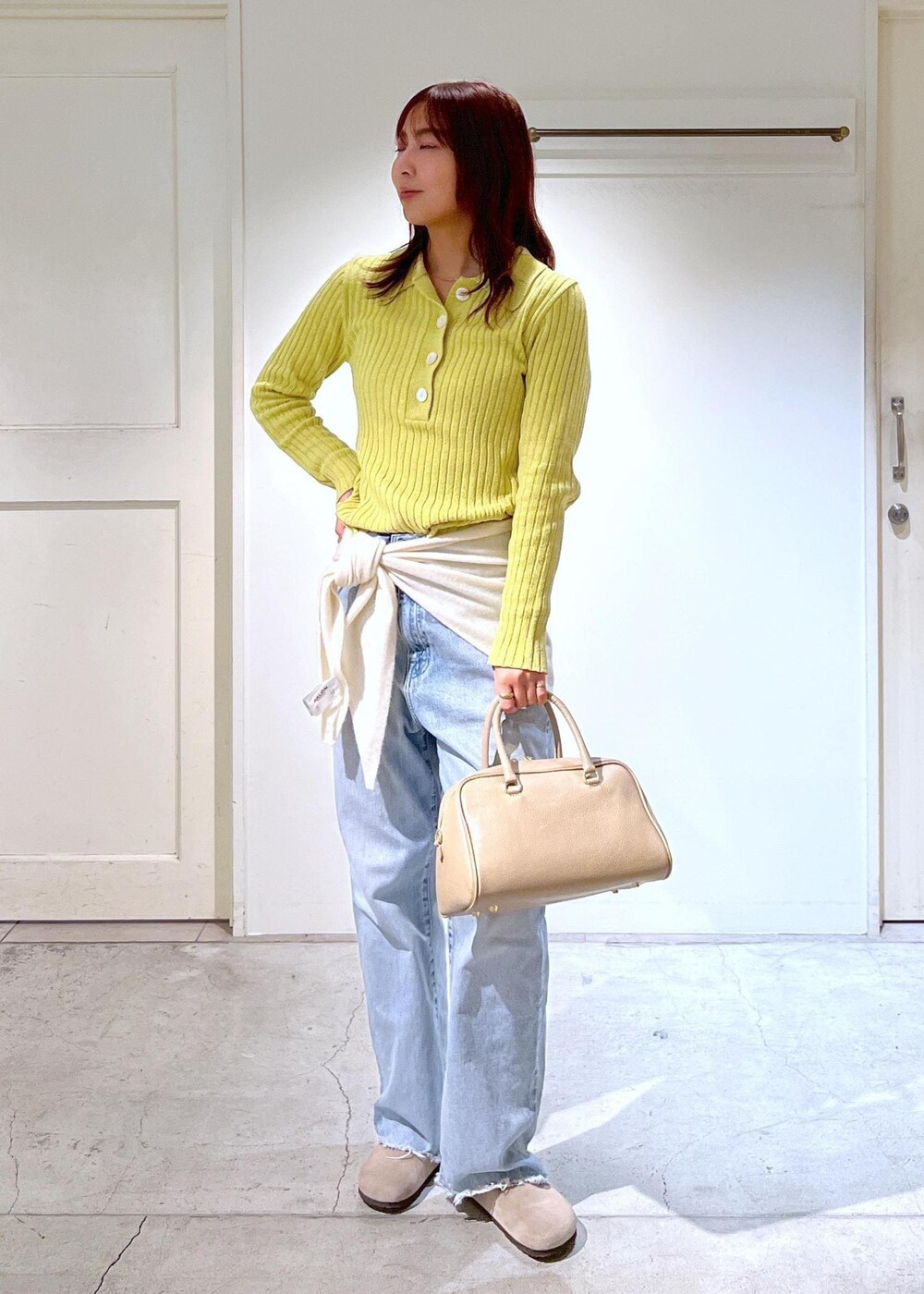 ベージュ系のボストンバッグ、イエロー系のニット/セーター、ブルー系のデニムパンツを着用したレディースの冬コーディネートの2枚目の写真