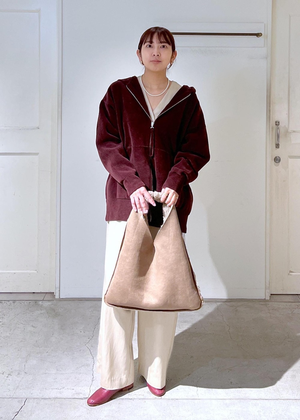 レッド系のパンプス、ブラウン系のパーカー、ベージュ系のトートバッグを着用したレディースの冬コーディネートの2枚目の写真