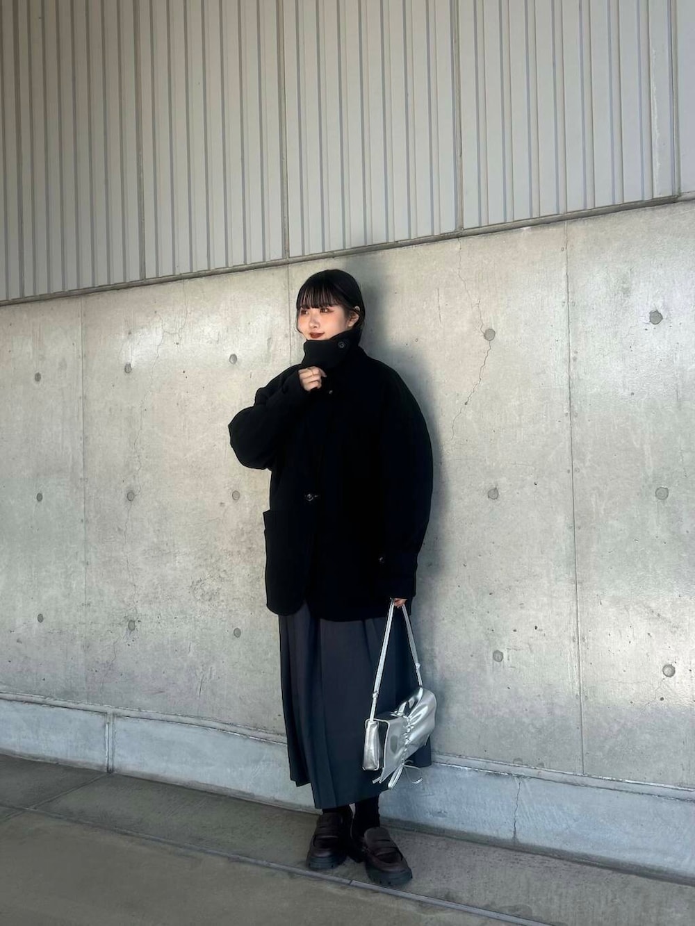 ブラック系のステンカラーコート、グレー系のワンピース、シルバー系のショルダーバッグを着用したレディースの冬コーディネートの2枚目の写真
