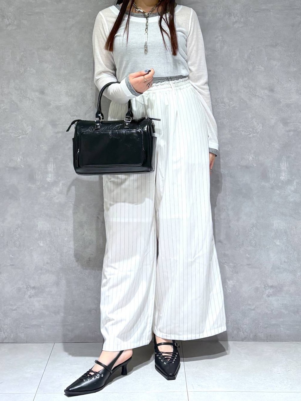 ブラック系のショルダーバッグ、ブラック系のサンダル、ホワイト系のスラックスを着用したレディースの冬コーディネートの2枚目の写真