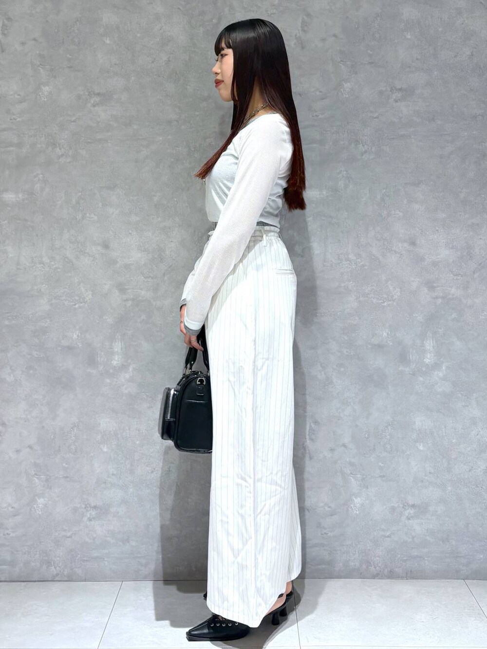 ブラック系のショルダーバッグ、ブラック系のサンダル、ホワイト系のスラックスを着用したレディースの冬コーディネートの3枚目の写真