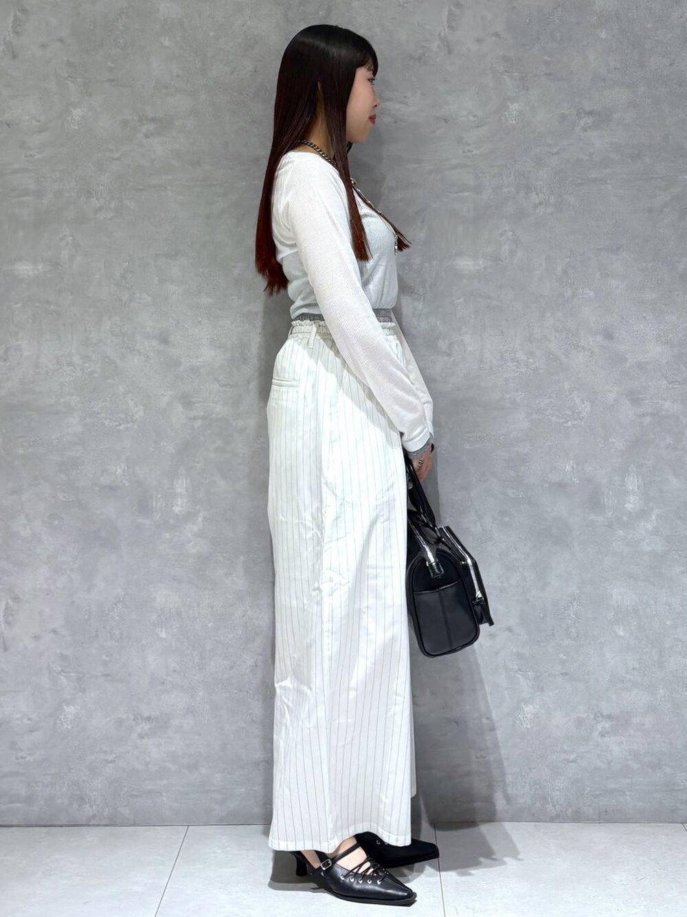 ブラック系のショルダーバッグ、ブラック系のサンダル、ホワイト系のスラックスを着用したレディースの冬コーディネートの5枚目の写真