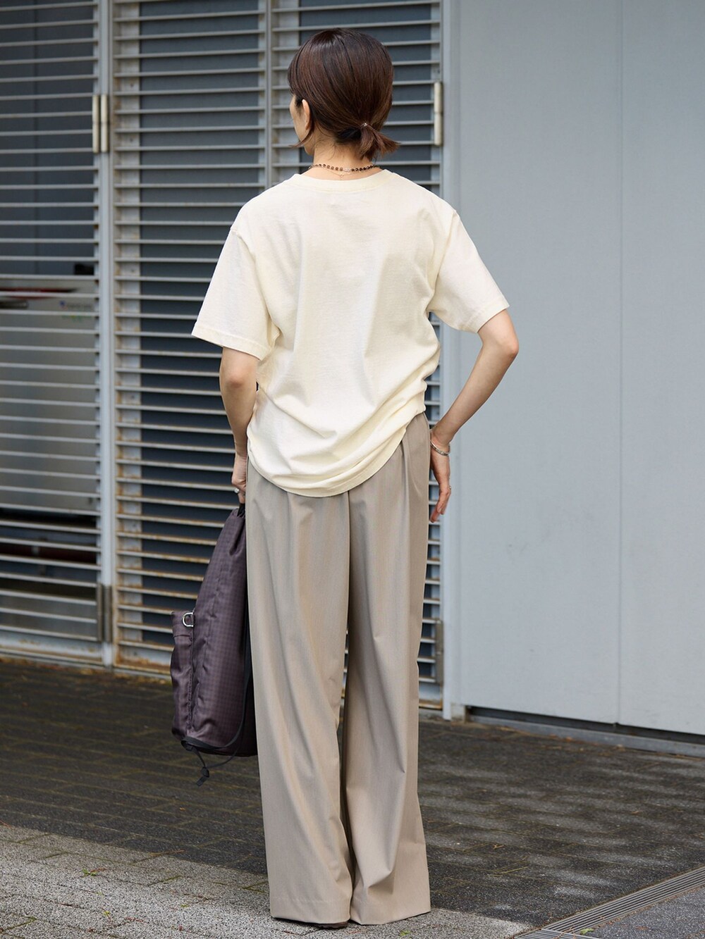 ベージュ系のスラックス、ホワイト系のTシャツ/カットソー、ブラウン系のバックパック/リュックを着用したレディースの夏コーディネートの2枚目の写真
