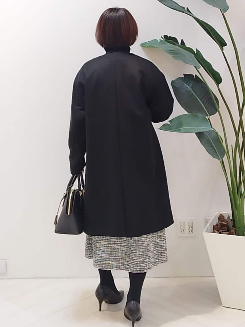 ブラック系のノーカラーコート、ブラック系のTシャツ/カットソー、ブラック系のスカートを着用したレディースの冬コーディネートの7枚目の写真
