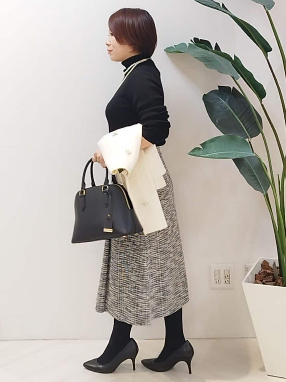 ブラック系のニット/セーター、ブラック系のスカート、ホワイト系のカーディガン/ボレロを着用したレディースの秋コーディネートの5枚目の写真