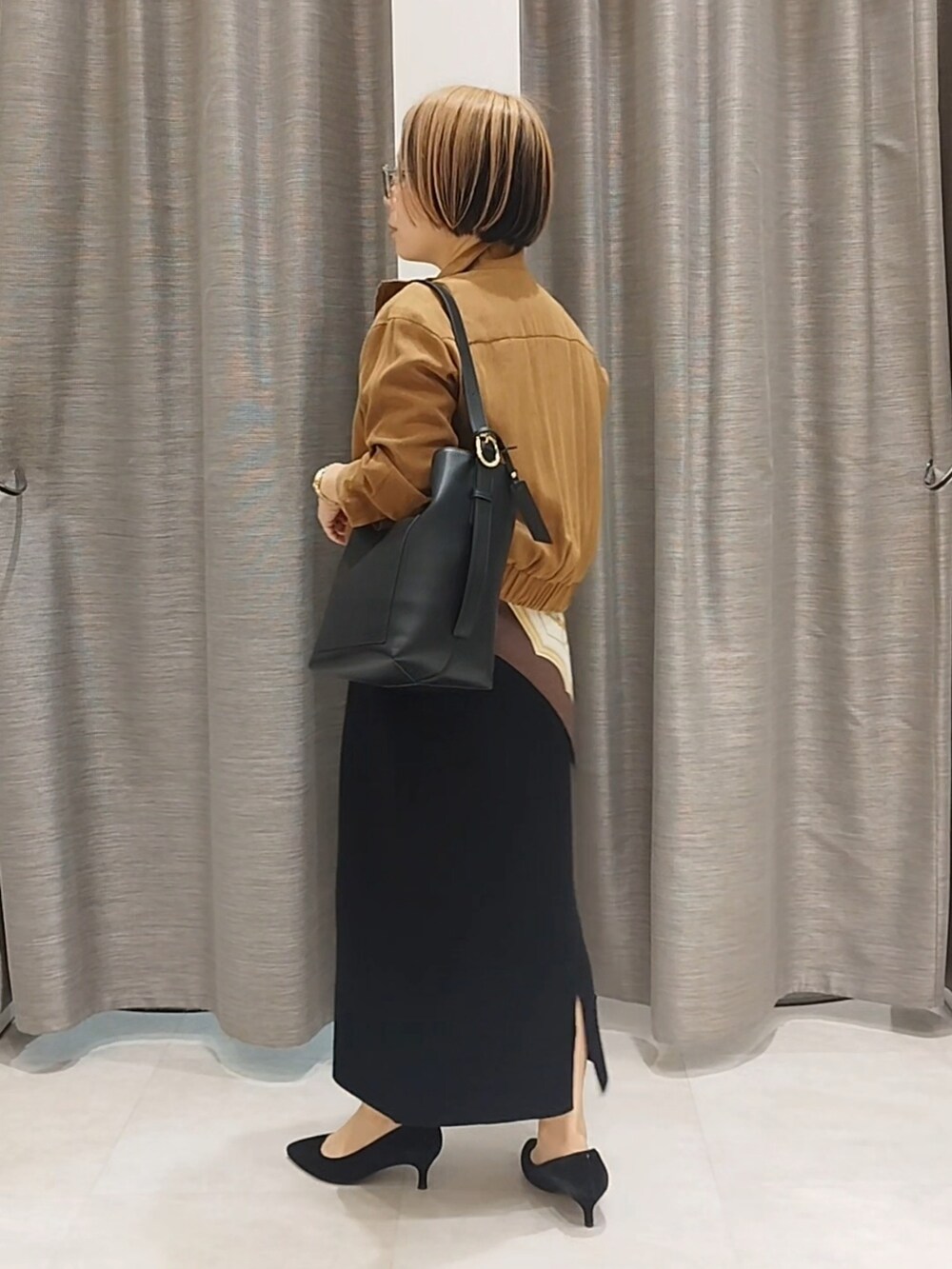 イエロー系のブルゾン、ブラック系のニット/セーター、ブラック系のスカートを着用したレディースの秋コーディネートの6枚目の写真